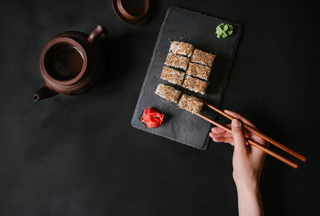 Using chosticks with sushi roll and tea